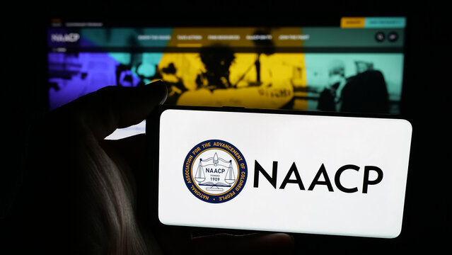 Stuttgart, Germany - 11-19-2025: Person holding mobile phone with logo of US colored people association NAACP on screen in front of web page. Focus on phone display.