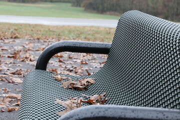 Black metal mesh public park bench covered in fallen autumn leaves