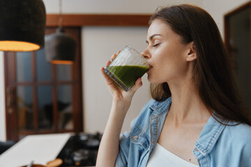 Young woman enjoying a healthy green smoothie in a modern kitchen, showcasing seasonal wellness and lifestyle choices