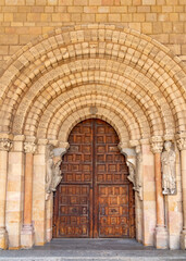 Close-up of Basílica de San Vicente’s Romanesque portal with a large rounded arch, sculpted archivolts on sturdy columns, and massive, richly patterned wooden doors