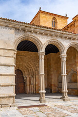 A large Romanesque church in Ávila, featuring a long arcaded portico with rounded arches and a warm golden stone exterior, standing prominently beneath a cloudy sky