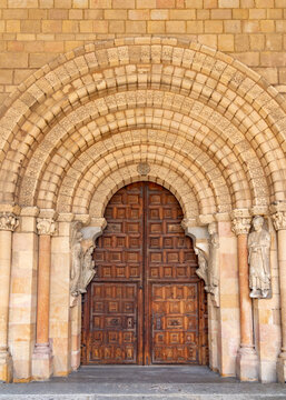 Close-up of Bas&iacute;lica de San Vicente&rsquo;s Romanesque portal with a large rounded arch, sculpted archivolts on sturdy columns, and massive, richly patterned wooden doors