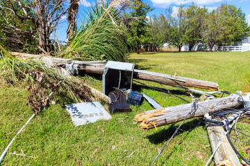 Utility equipment lies damaged on grass after hurricane storm, surrounded by fallen tree branches scattered debris.