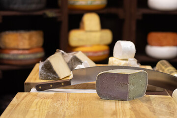 Assorted cheese blocks and knife on wooden board in a rustic cheese shop display