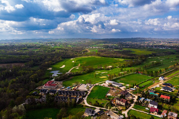 Wide aerial drone panorama of a lush green golf course on a bright, cloudy day. Featuring fairways, sand traps, and luxury resort facilities in the distance.