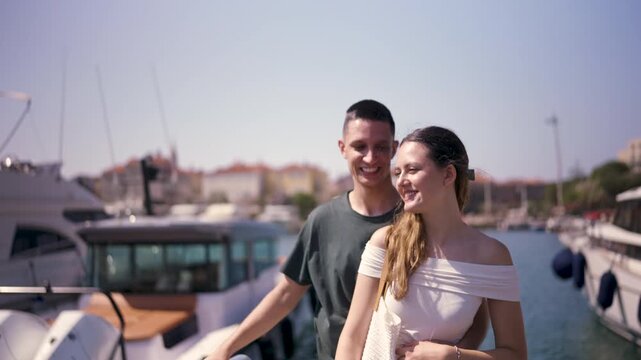 A young couple walks side by side along a seaside marina, enjoying a peaceful moment by the water