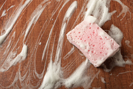 Cleaning a wooden surface with pink sponge and soap foam for a sparkling finish