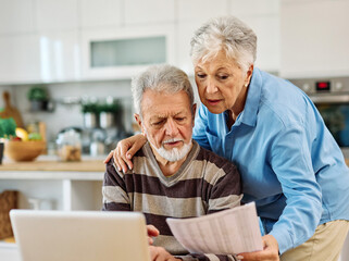 Senior couple checking bills and calculating expenses using a laptop at home, debt taxes concept, worried married elderly couple