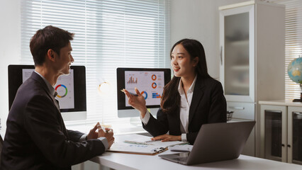 Business professionals collaborating in an office, reviewing charts and graphs on computer screens, having a productive discussion