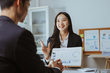 Smiling Asian businesswoman presenting financial charts and data to a male client, discussing strategy during an office meeting
