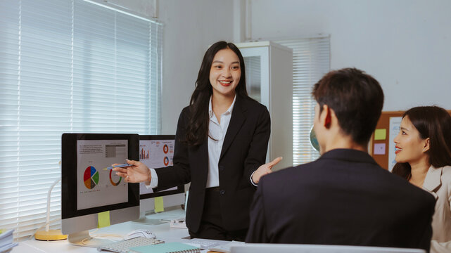 Confident businesswoman presenting data analysis to her team using computer screens, fostering collaboration and project discussion