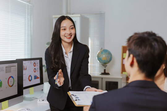 Businesswoman presenting financial data on a clipboard, engaging in a professional office discussion with colleagues, showing teamwork