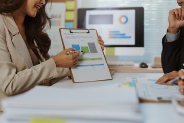 Business people analyzing charts, budgets, and financial data on documents and a computer monitor, collaborating in a modern office