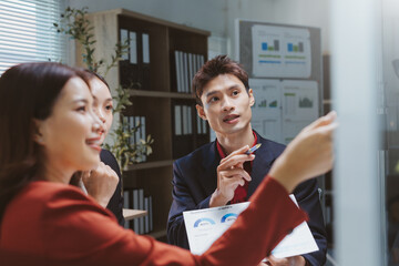 Asian business professionals engaging in a meeting, analyzing charts and discussing strategies for collaboration and teamwork in the office