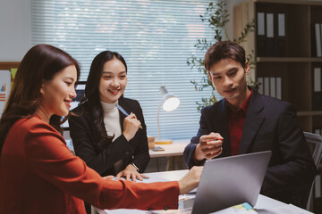 Professional Asian business colleagues discussing strategy and planning future goals around a laptop in a modern office