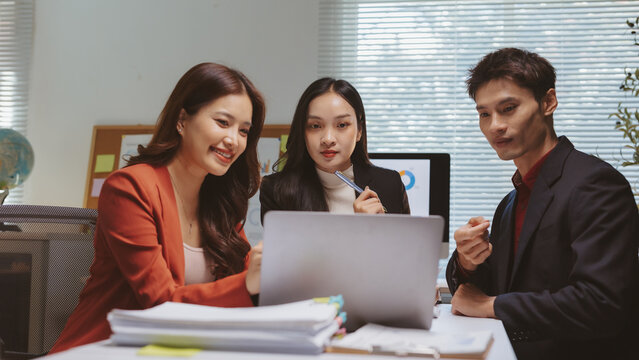 Asian business professionals brainstorming and discussing project strategy, viewing data and charts on a computer in a corporate setting