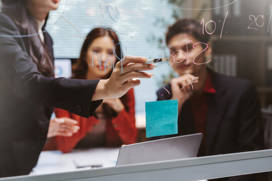 Business team members collaborating, discussing, and planning new strategies on a transparent glass board with financial data