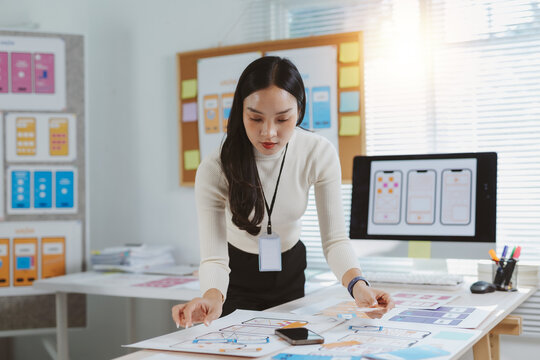 Asian woman analyzing mobile application wireframe layouts and user interface flow, developing new technology experiences