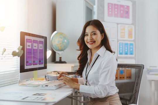 Asian woman smiling and working on web and mobile app UIUX design on her computer in creative office - Powered by Adobe
