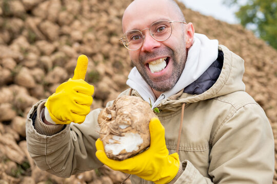 Cheerful Playful young farmer playfully biting into piece freshly harvested sugar beet, tasting crop, healthy eating, genuine smile, agricultural harvest joy, examining sweet freshness root vegetable - Powered by Adobe