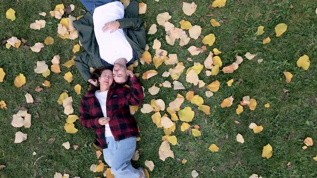 Multicultural couple lying on autumn leaves smiling and cuddling outdoors.