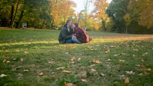 Romantic young multiracial couple enjoying a date in an autumn park, sitting on grass drinking tea.