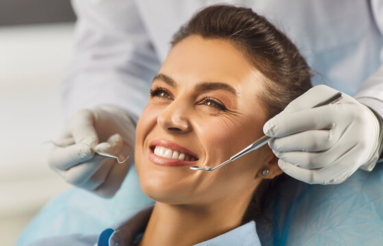 Close up portrait of smiling woman sitting in dental chair during checkup while dentist in gloves holding dental tools, ensuring proper oral care during regular medical check up in dentistry clinic.
