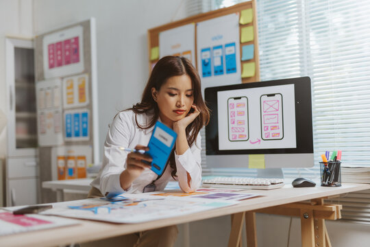Woman uiux designer analyzing smartphone app layout wireframe on computer screen at office desk, developing user experience
