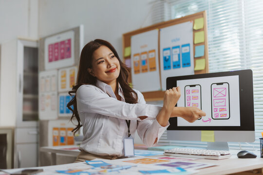 Young Asian female UX designer stretching arms, taking a break from designing mobile application wireframes in modern office