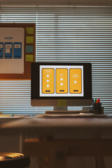 Desk with a computer screen displaying UIUX design mockups for mobile applications, illustrating the development process