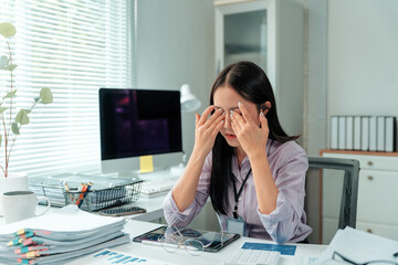 Overworked businesswoman rubbing tired eyes at her office desk, feeling stress and burnout from long hours and computer work