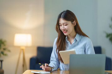 Young Asian woman working from home, smiling while calculating personal finances and managing her budget