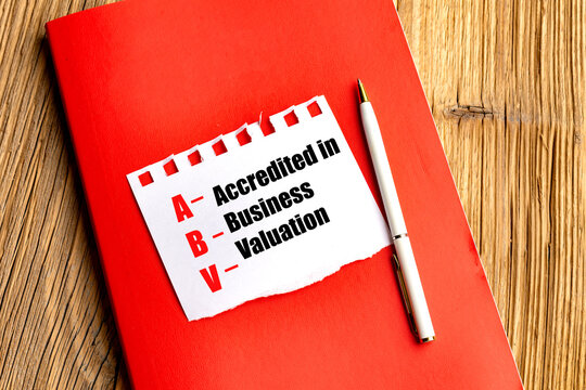 ABV acronym meaning accredited in business valuation on paper note with pen on red notebook