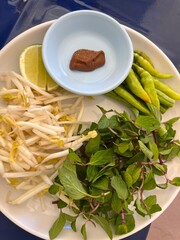 A plate of fresh garnishes and condiments commonly served with Southeast Asian noodle soups, particularly Vietnamese Phở or certain Thai and Lao dishes.