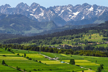 Panoramic view of the snow-capped Tatra Mountains from Rzepiska village in Podhale, Poland. Scenic June landscape with vivid green fields and rural settlement.