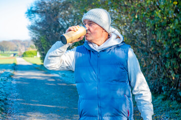 senior male runner in sportswear taking break during morning run drinking warm beverage, hot drink...