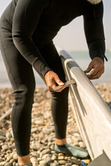 Person attaching fin to paddle board on beach