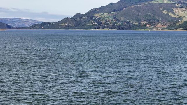 Plano general sobrevolando la laguna de Tomin&eacute; en Cundinamarca - Colombia, mostrando el agua azul de la laguna, con el paisaje y los bosques verdes de la monta&ntilde;a que la rodea.