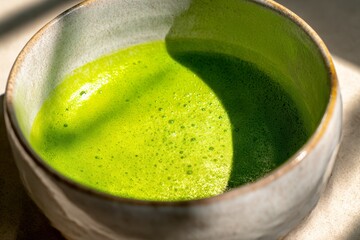 Matcha tea in a beautiful ceramic bowl, close up of a traditional japanese green drink with foam and bright sunlight
