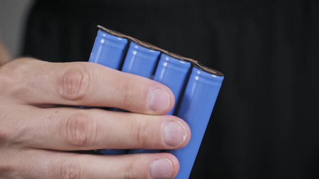 Close-up shot of a hand rotating a custom-made battery pack of four blue li-ion cells showing the spot-welded nickel strips on the terminals for a power source.