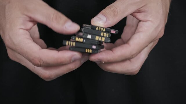 Close-up of hands holding and sorting through a stack of old used lithium-ion batteries from mobile phones highlighting e-waste and the need for battery recycling.