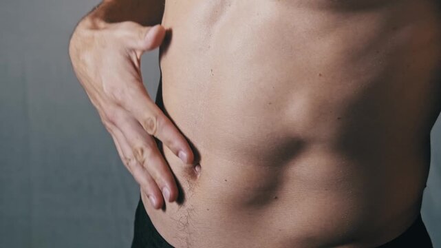 A close-up side shot of a man's athletic torso. He runs his hand along his side, feeling the definition of his oblique and abdominal muscles, assessing the results of his fitness training.