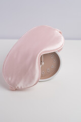 Alarm clock partially covered by pink silk sleep mask. Prioritizing rest.	