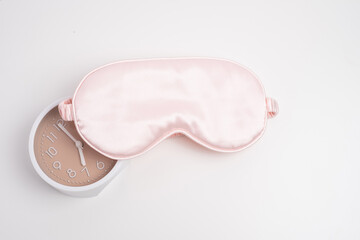 Alarm clock partially covered by pink silk sleep mask. Prioritizing rest.	