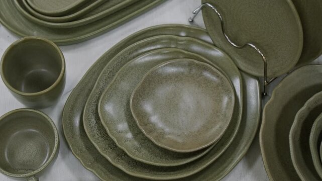 No people top view of stylish set of khaki green earthen or ceramic dinnerware set, various size of plates, dishes, bowls, cups arranged on merchandise display table at tableware store