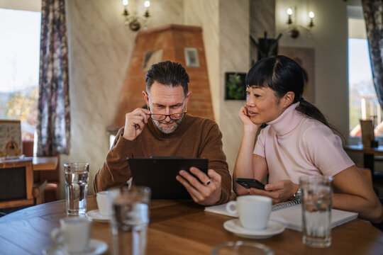 Mature business colleagues discussing planning using digital tablet in cafe