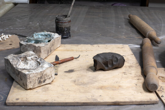 Lump of clay and molding tools on wooden board in workshop. Artisan craft, pottery, sculpting process. Real photo