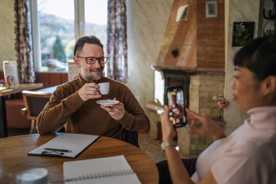 Woman taking smart phone recording of man having coffee