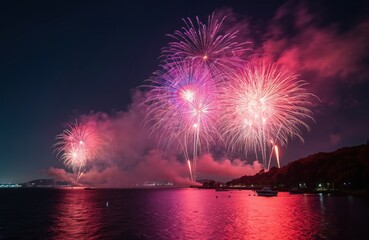 Fototapeta premium Colorful fireworks explode over sea on festive night. Pyrotechnic show illuminates dark sky with vibrant light. Celebration display reflects on water near coastal city during national holiday.