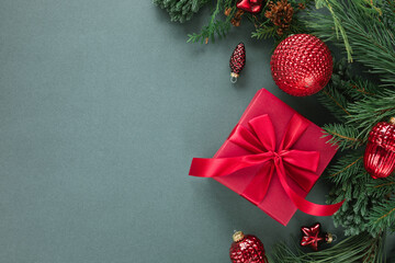 Overhead view of a wrapped Christmas gift box, festive Christmas baubles and ornaments with fir branches on a green background